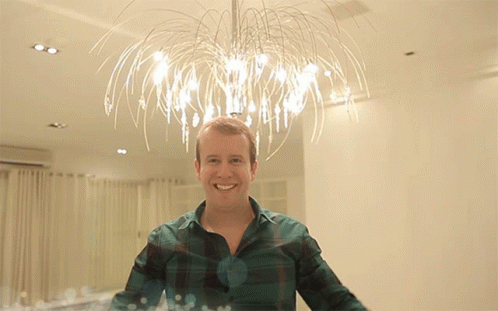 Man In Plaid Shirt Smiling In Front Of Chandelier GIF
