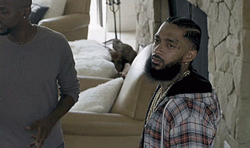 A Man In A Plaid Shirt Stands Next To Another Man In A Living Room GIF