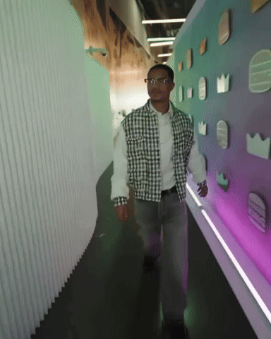 Man In Plaid Shirt Walking Down Hallway With Purple Wall GIF