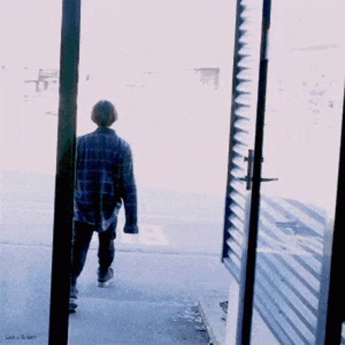A Man In A Plaid Shirt Walks Down The Street GIF