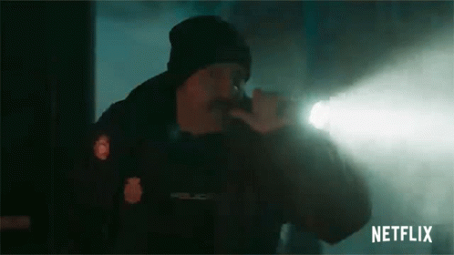 A Man In A Police Uniform Is Holding A Flashlight In His Hand . GIF