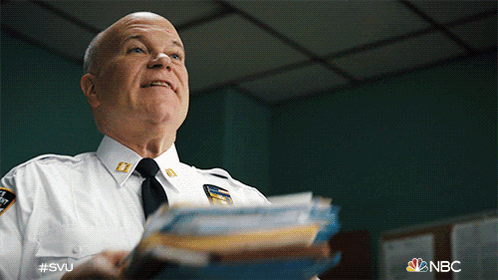 A Man In A Police Uniform Is Holding A Stack Of Papers In His Hand GIF