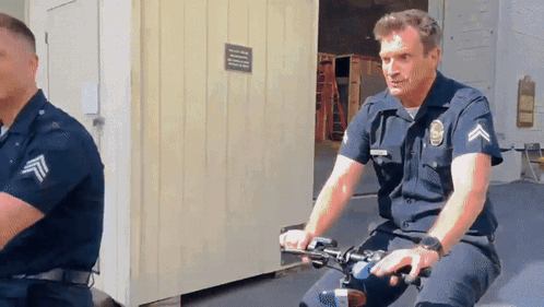 A Man In A Police Uniform Is Riding A Bike In Front Of A Building GIF