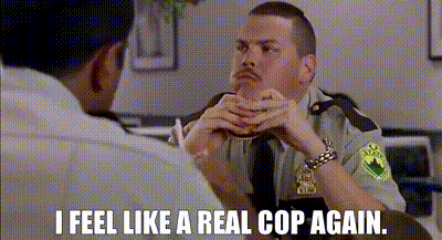 A Man In A Police Uniform Is Sitting At A Table With Another Man And Eating A Hamburger . GIF