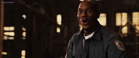 A Man In A Police Uniform Is Standing In A Dark Room Holding His Fist Up . GIF