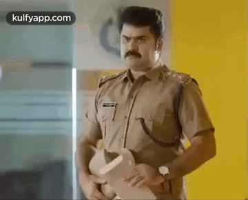 A Man In A Police Uniform Is Standing In A Room Holding A Hat . GIF