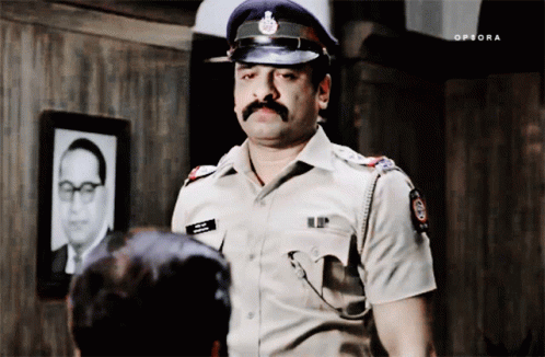 A Man In A Police Uniform Is Standing In Front Of A Picture Of A Man With A Mustache GIF