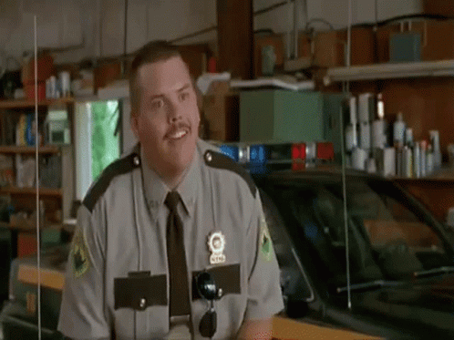 A Man In A Police Uniform Is Standing In Front Of A Police Car . GIF