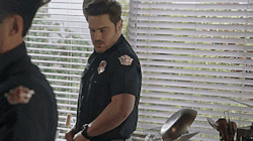 A Man In A Police Uniform Is Standing In Front Of A Window GIF