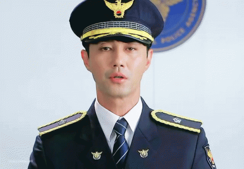 A Man In A Police Uniform Stands In Front Of A Police Logo GIF