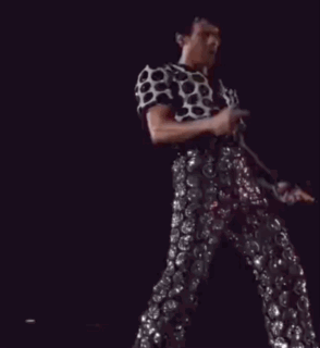 A Man In A Polka Dot Shirt And Sequined Pants Is Dancing On Stage GIF