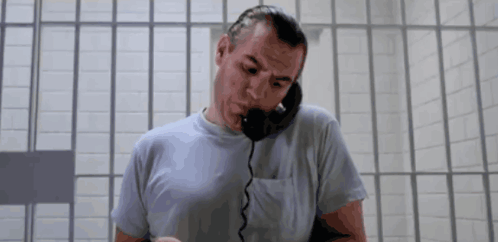 A Man In A Prison Cell Talking On A Phone GIF