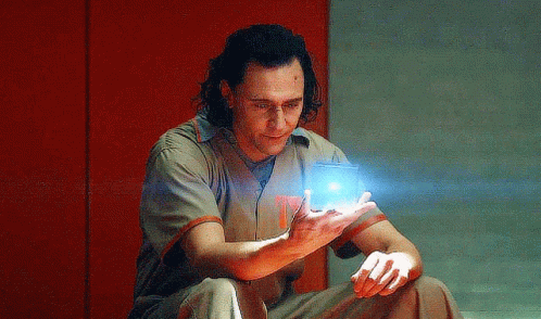 A Man In A Prison Uniform Is Sitting On The Floor Holding A Blue Object In His Hand . GIF