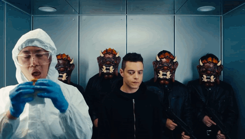 A Man In A Protective Suit Is Eating A Hamburger In Front Of A Group Of Men Wearing Masks GIF