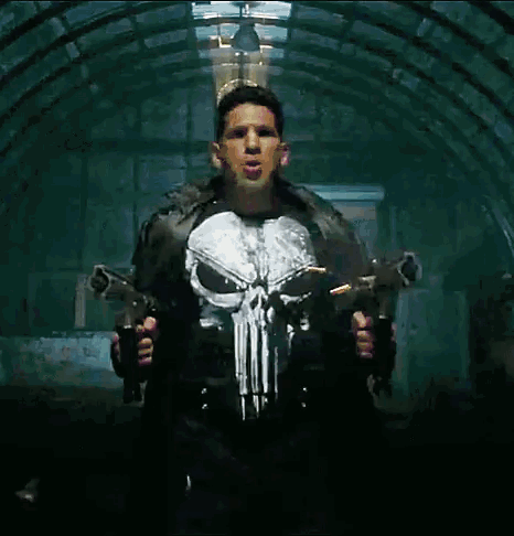 A Man In A Punisher Costume Holds Two Guns GIF