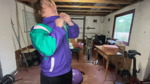 A Man In A Purple And Green Jacket Is Standing In A Garage With A Box That Says Ebay GIF