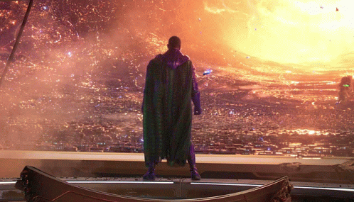 A Man In A Purple Cape Is Standing In Front Of A Fire GIF