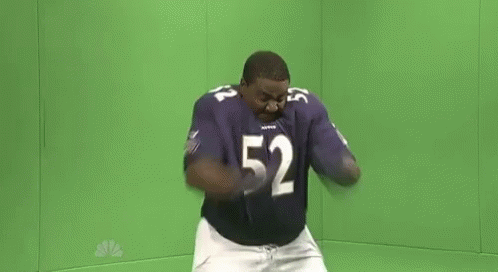 A Man In A Purple Football Uniform Is Dancing In Front Of A Green Screen . GIF