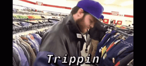 A Man In A Purple Hat Is Looking At Clothes In A Store And The Word Trippin Is On The Screen GIF