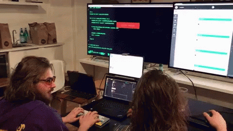 A Man In A Purple Hoodie Is Typing On A Keyboard In Front Of A Computer Monitor GIF
