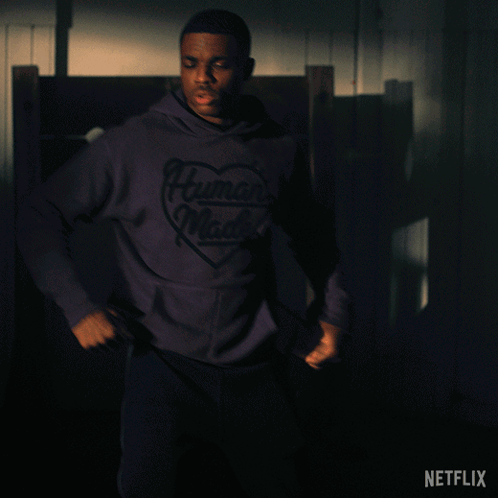 A Man In A Purple Human Made Hoodie Stands In A Dark Room GIF