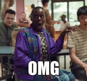 A Man In A Purple Jacket And Tie Is Sitting At A Table With Other People And Making A Surprised Face . GIF