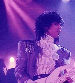 A Man In A Purple Jacket And White Shirt Is Playing A Guitar On Stage . GIF