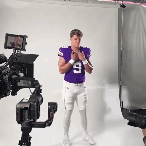 A Man In A Purple Jersey With The Number 3 On It Stands In Front Of A Camera GIF