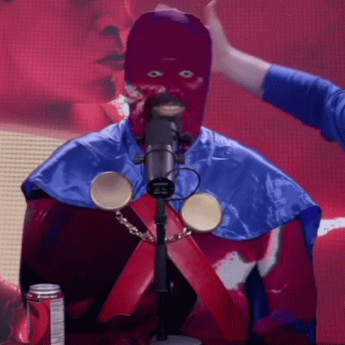 A Man In A Purple Mask Is Standing In Front Of A Microphone With A Can Of Dr Pepper In The Background GIF