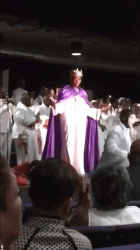 A Man In A Purple Robe And Crown Is Standing In Front Of A Crowd GIF