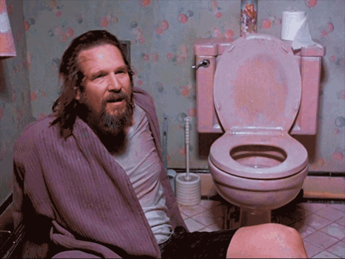A Man In A Purple Robe Sits In A Pink Toilet GIF