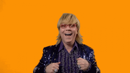 A Man In A Purple Sequined Jacket Holds His Hands Up In The Air With The Words Swipe Up Below Him GIF