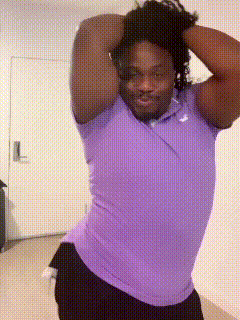 a man in a purple shirt and black shorts is standing in front of a door