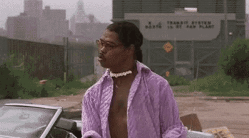A Man In A Purple Shirt And Choker Is Standing Next To A Car . GIF
