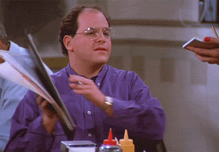 A Man In A Purple Shirt And Glasses Is Holding A Menu GIF