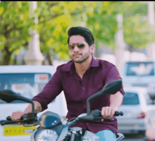 A Man In A Purple Shirt And Sunglasses Is Riding A Motorcycle GIF