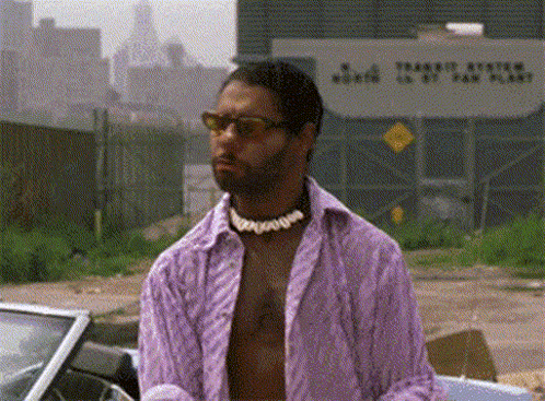 A Man In A Purple Shirt And Sunglasses Is Standing In Front Of A Car . GIF