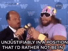 A Man In A Purple Shirt And Sunglasses Is Talking Into A Microphone While Another Man Looks On . GIF