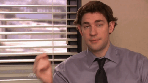 A Man In A Purple Shirt And Tie Is Sitting In Front Of A Window With Blinds GIF