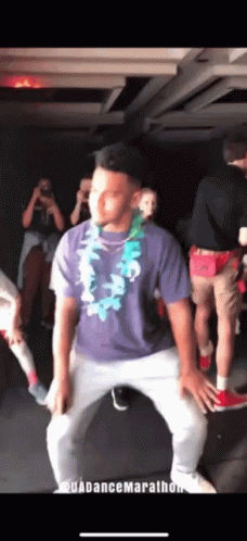 A Man In A Purple Shirt And White Pants Is Dancing In A Dark Room GIF