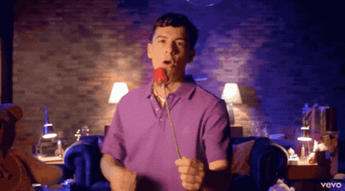 A Man In A Purple Shirt Holds A Rose In His Mouth GIF