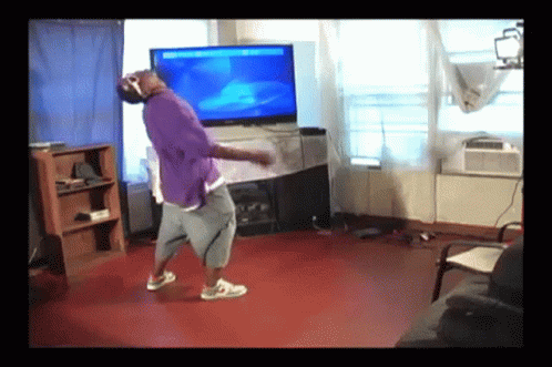 a man in a purple shirt is dancing in front of a flat screen television