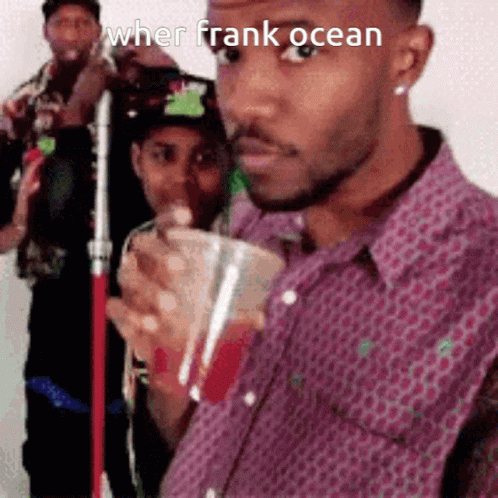 A Man In A Purple Shirt Is Drinking From A Cup While Standing In Front Of A Group Of People . GIF