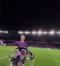 a man in a purple shirt is holding a soccer ball on a field at night
