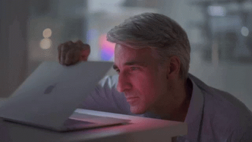 A Man In A Purple Shirt Is Looking At A Laptop GIF