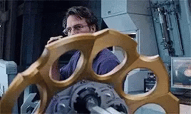 A Man In A Purple Shirt Is Looking At A Large Gold Object In A Room . GIF