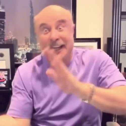 A Man In A Purple Shirt Is Making A Funny Face While Sitting At A Table . GIF