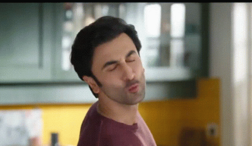 A Man In A Purple Shirt Is Making A Funny Face With His Eyes Closed . GIF