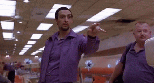 A Man In A Purple Shirt Is Pointing At Something While Standing Next To Another Man . GIF