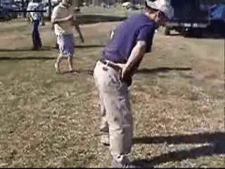 A Man In A Purple Shirt Is Standing In The Grass With His Hands On His Hips . GIF
